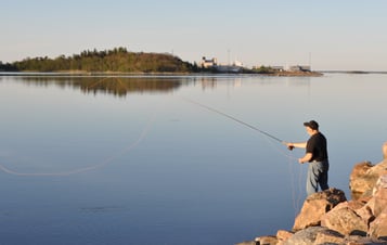 Man fishing from rocks, with Forsmark visible across the water