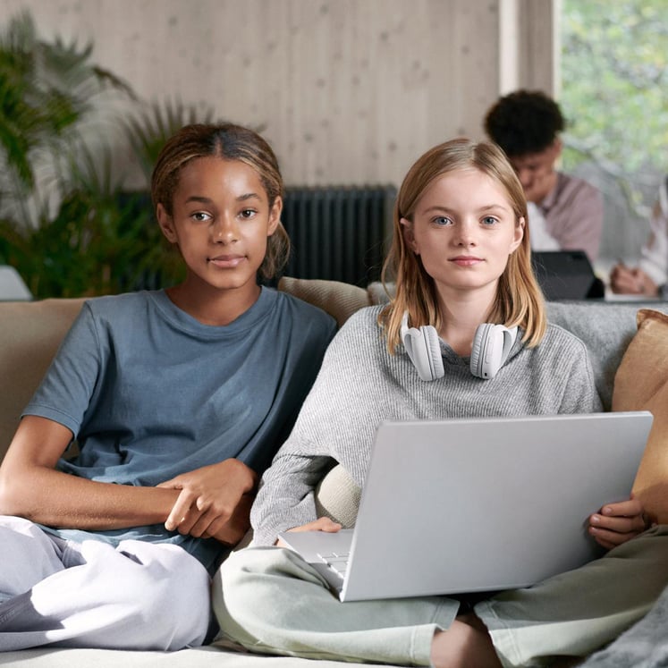 Två flickor som sitter i en soffa med en laptop och tittar in i kameran. Två flickor som sitter i en soffa med en laptop och tittar in i kameran.