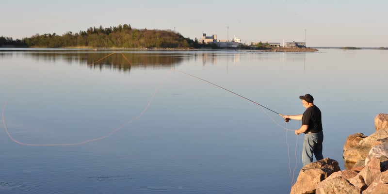 Man fishing from rocks, with Forsmark visible across the water