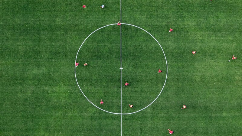 Flygbild över mittcirkeln på en fotbollsplan med spelare utspridda på gräset. Flygbild över mittcirkeln på en fotbollsplan med spelare utspridda på gräset.