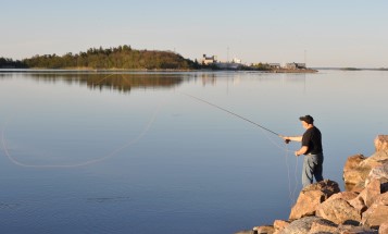 Man fishing from rocks, with Forsmark visible across the water